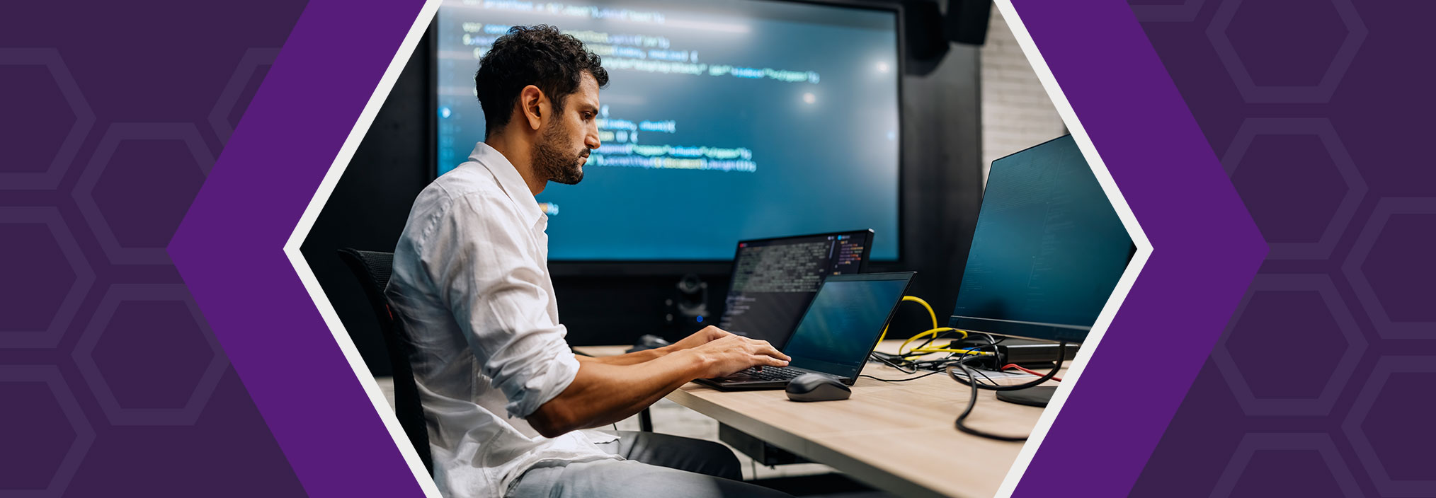 Person typing on a laptop with code on large screens in a modern office.