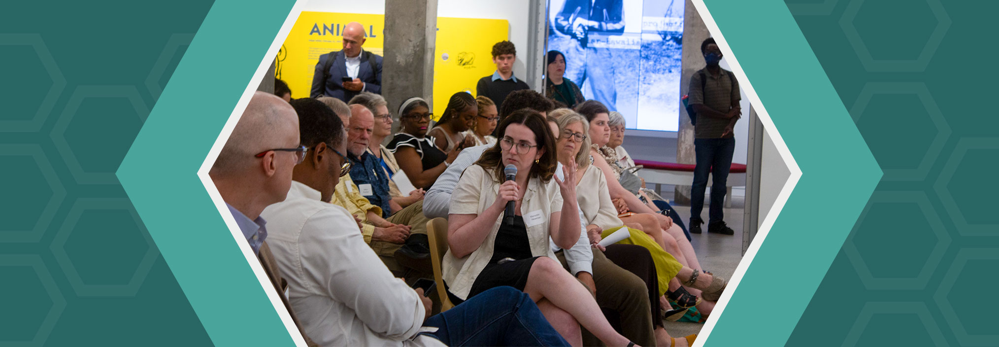 A woman speaks into a microphone among a diverse group seated in a discussion setting.