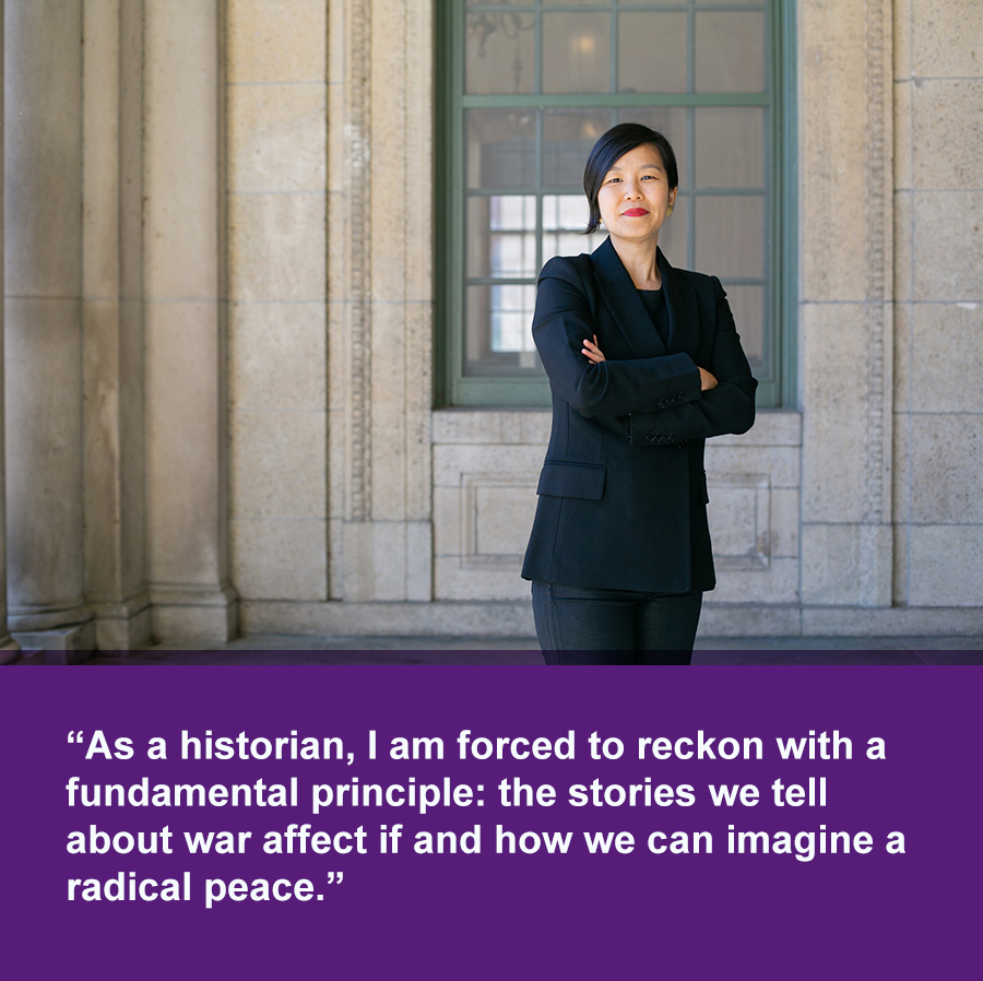 An smiling Asian woman stands in front of a stone building with large pillars and multi-paned window