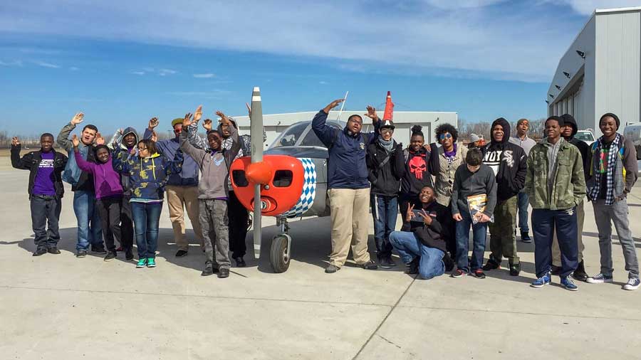 A group of youth standing in front of a prop plane at AeroStar Avion Institute, youth apprentices