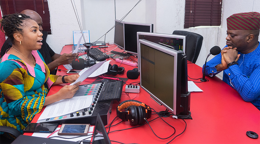 Black man and woman in traditional African garments with microphones and radio production equipment