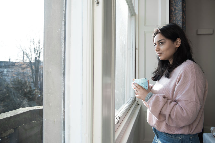 women holding a mug looking out a window