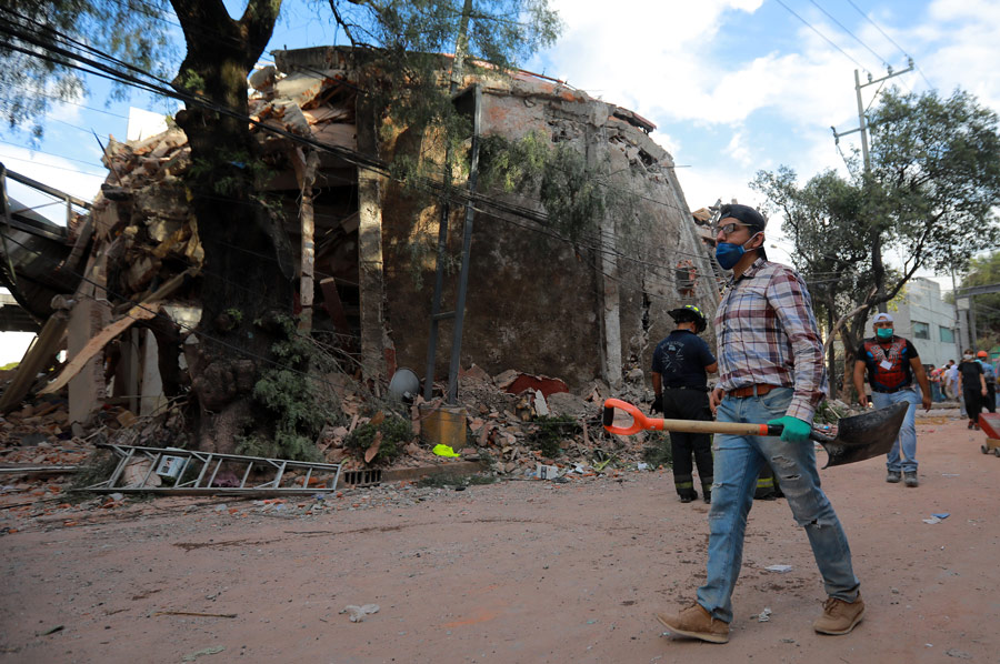 Man_With_Shovel_Walking_Down_Street_With_Collapsed_Buildings_And_Rubble