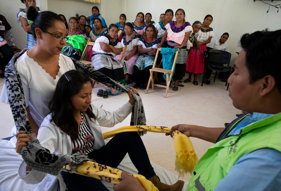 Group_Of_Mexican_Women_Watching_Instructor_Provide_Support_To_Pregnant_Woman's_Back_Using_Scarves