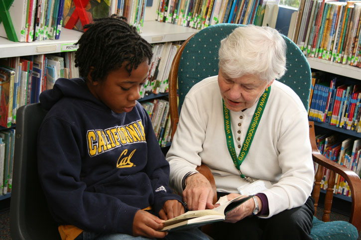 ElderlyWomanTutoringYoungStudentAtLibrary