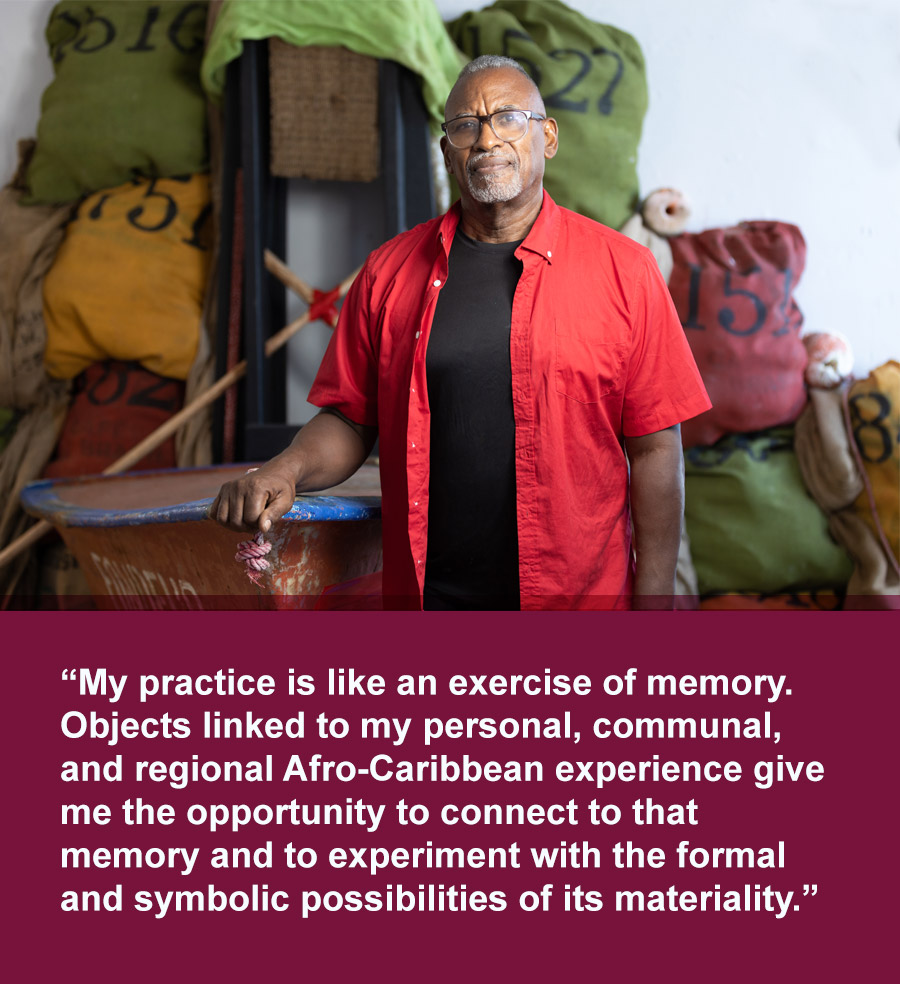 Latino man wearing glasses, red button-down shirt over black tee stands in front of sculpture made of brightly colored fabric sacks and the prow of a small boat. Quote text below reads: My practice is like an exercise of memory. Objects linked to my personal, communal, and regional Afro-Caribbean experience give me the opportunity to connect to that memory and to experiment with the formal and symbolic possibilities of its materiality.