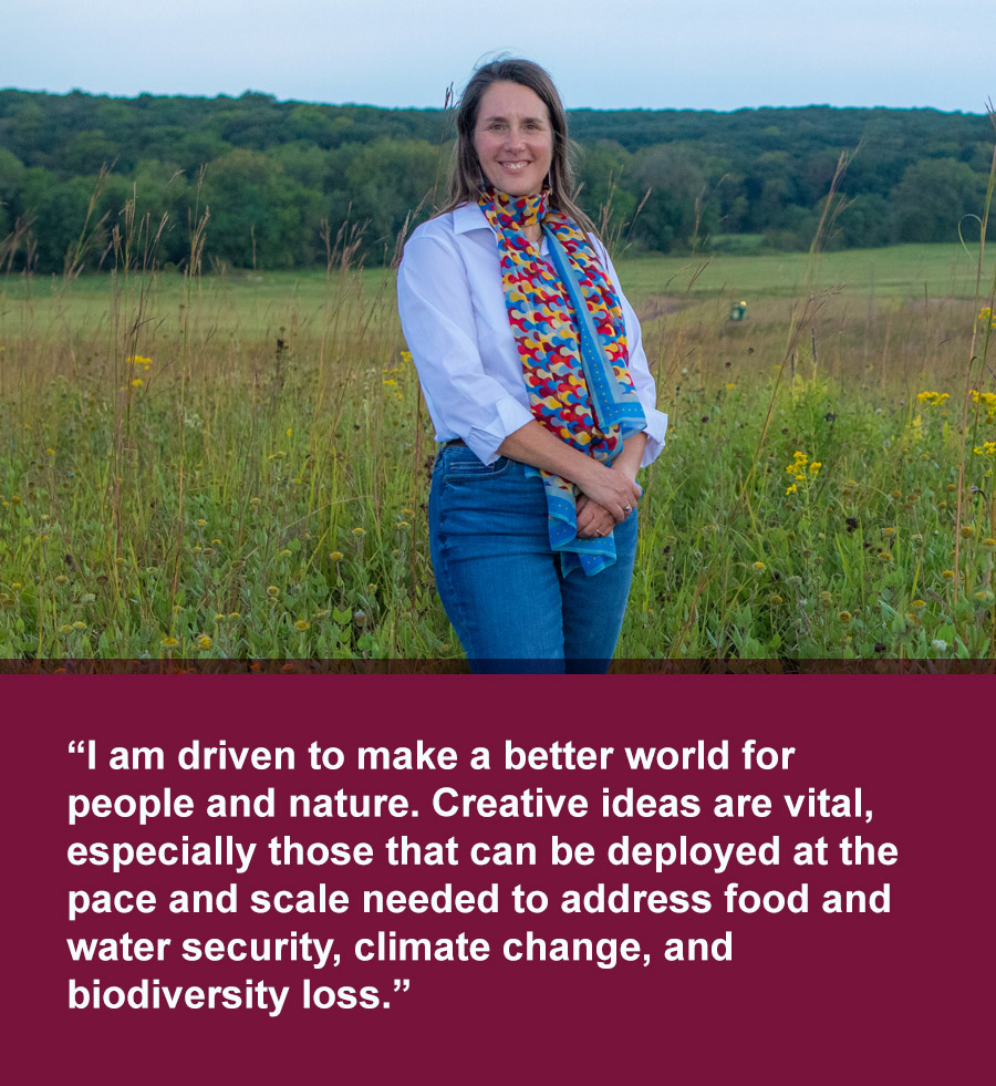 Middle aged white woman with long blonde hear wearing light blue button down and colorful patterned scarf stands in a pasture of tall native grasses. Quote text below photo reads: I am driven to make a better world for people and nature. Creative ideas are vital, especially those that can be deployed at the pace and scale needed to address food and water security, climate change, and biodiversity loss.