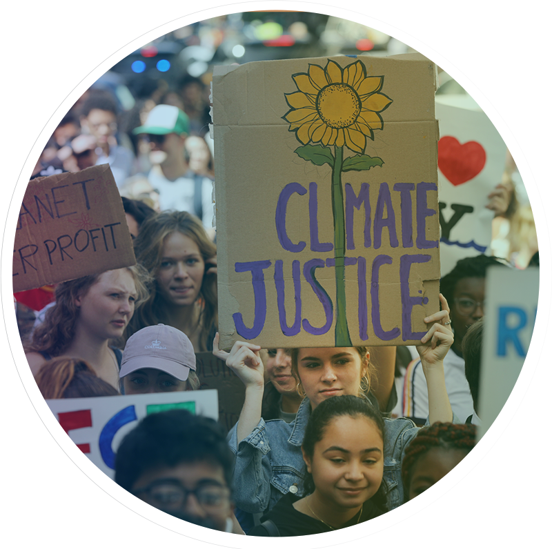Group of people at a rally, young woman holding a handmade sign with Climate Justice and a flower